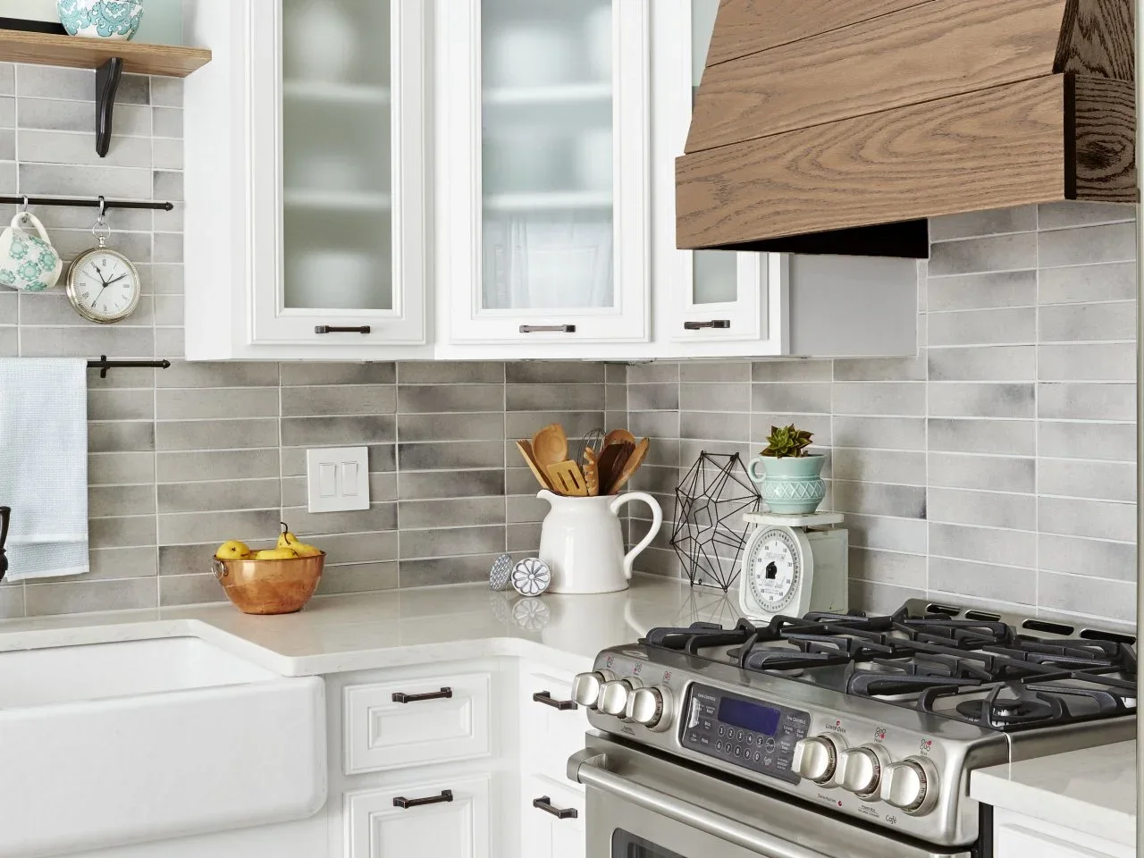 A broad wood hood sits beside white cabinets, gray rectangular tiles and a small timber display shelf.