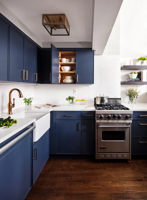 Navy cabinets wrap a compact kitchen below pale counters and a small timber-lined display niche.