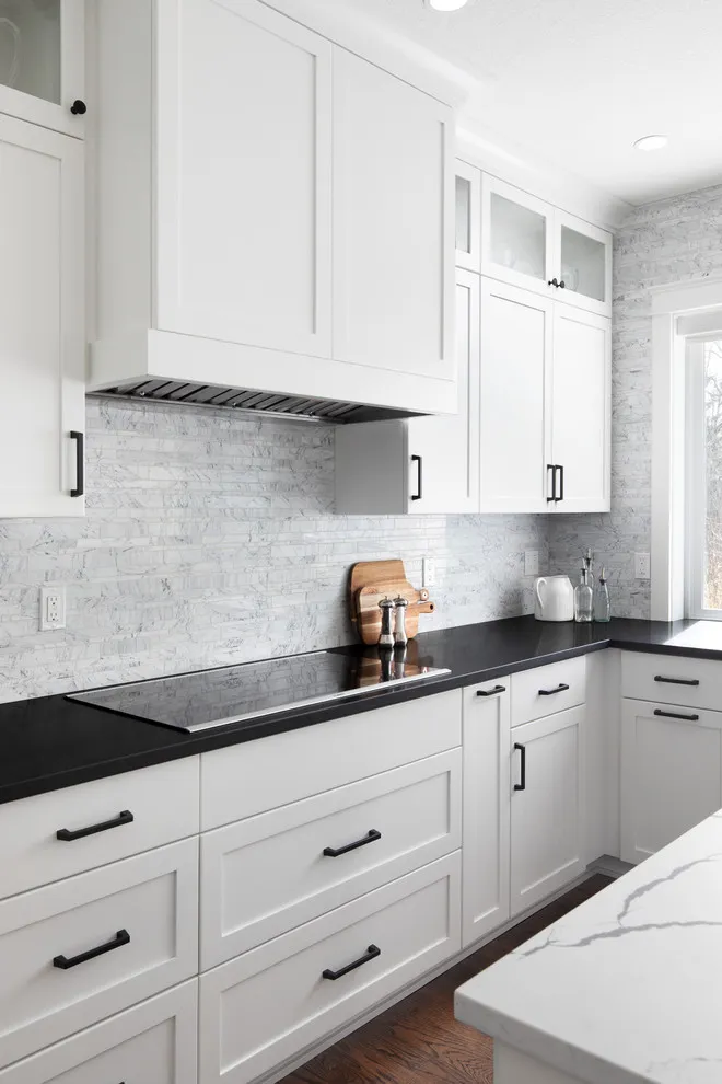 White cabinets meet dark worktops below a pale tiled backsplash in a compact kitchen