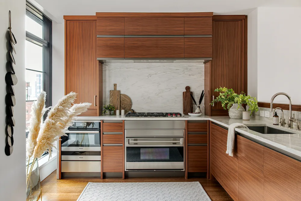 Reddish-brown kitchen cabinets surrounding a pale backsplash and range, with matching lower drawers and a window.