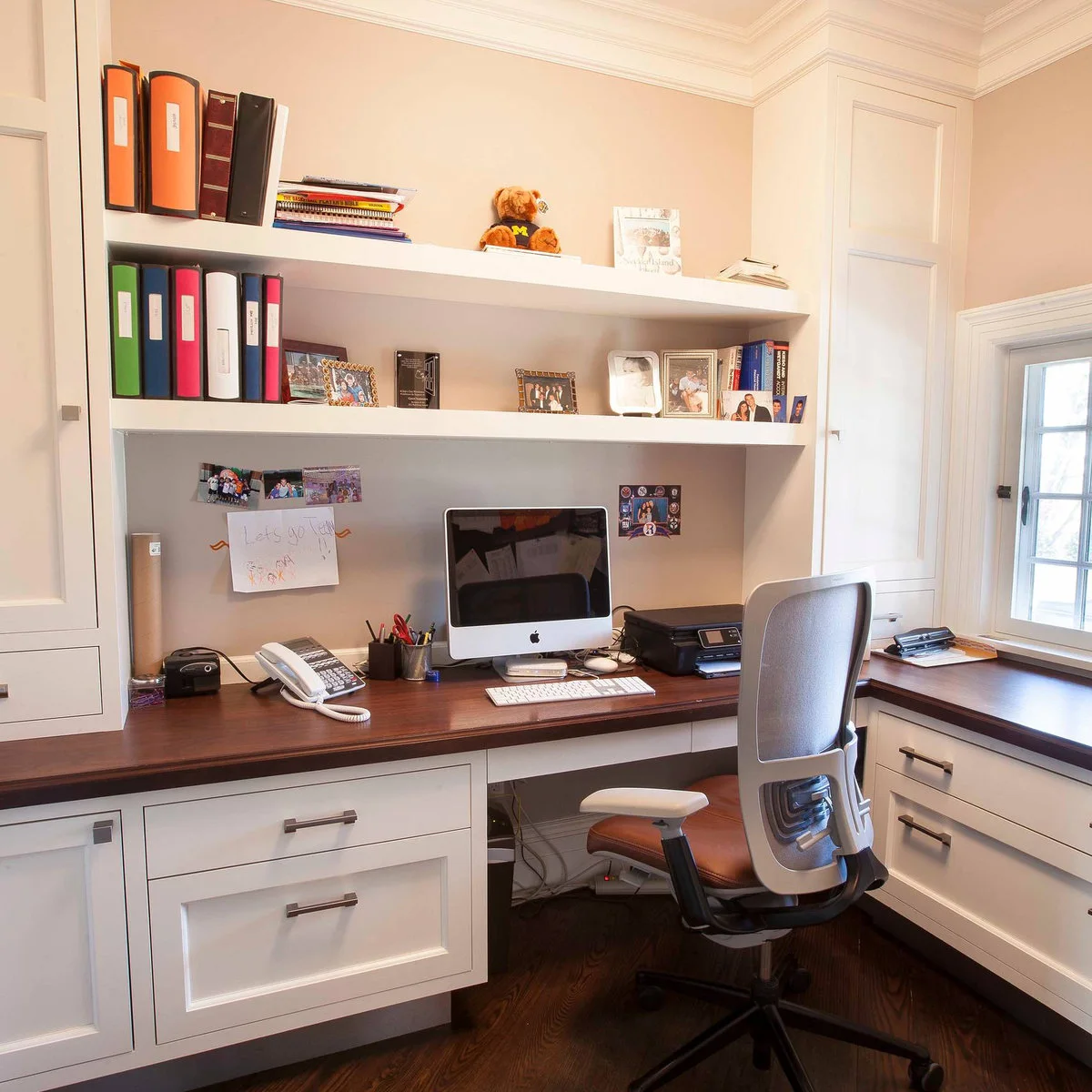 L-shaped wood-top desk with white drawers, a monitor, printer and an adjustable office chair