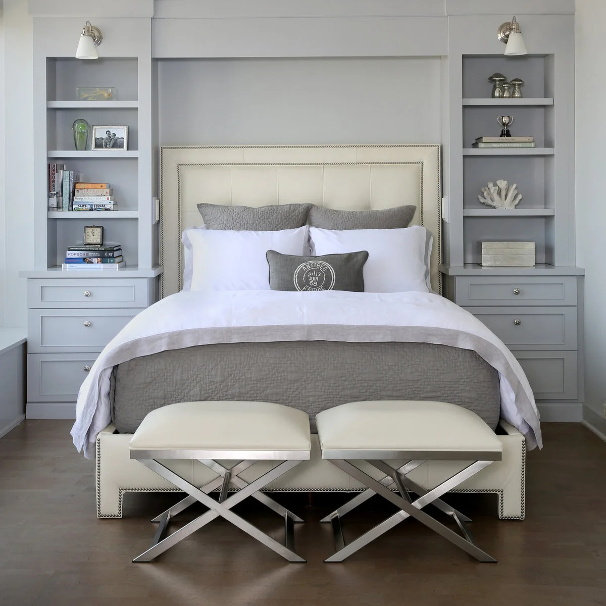 A pale bed set between two fitted gray drawer units and book shelves, with two small stools at the foot.