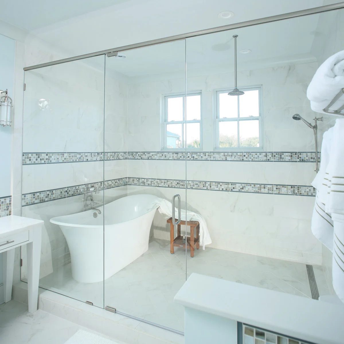 Freestanding tub and shower enclosed together behind glass with a long floor drain