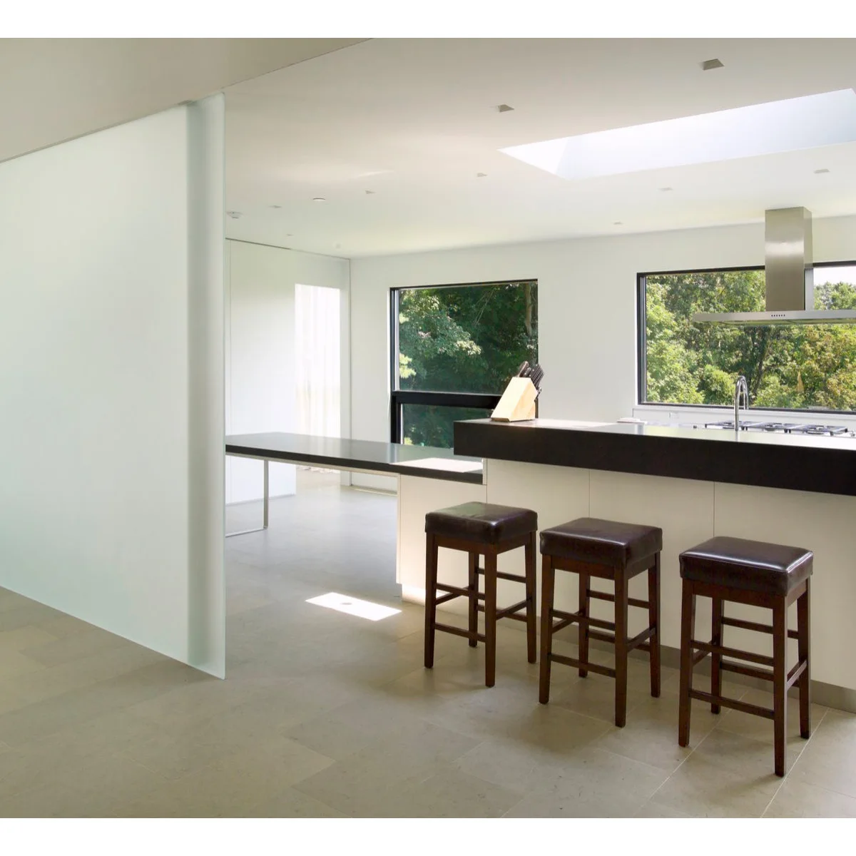 A large pale translucent screen stands beside a white kitchen with dark counters and three stools.