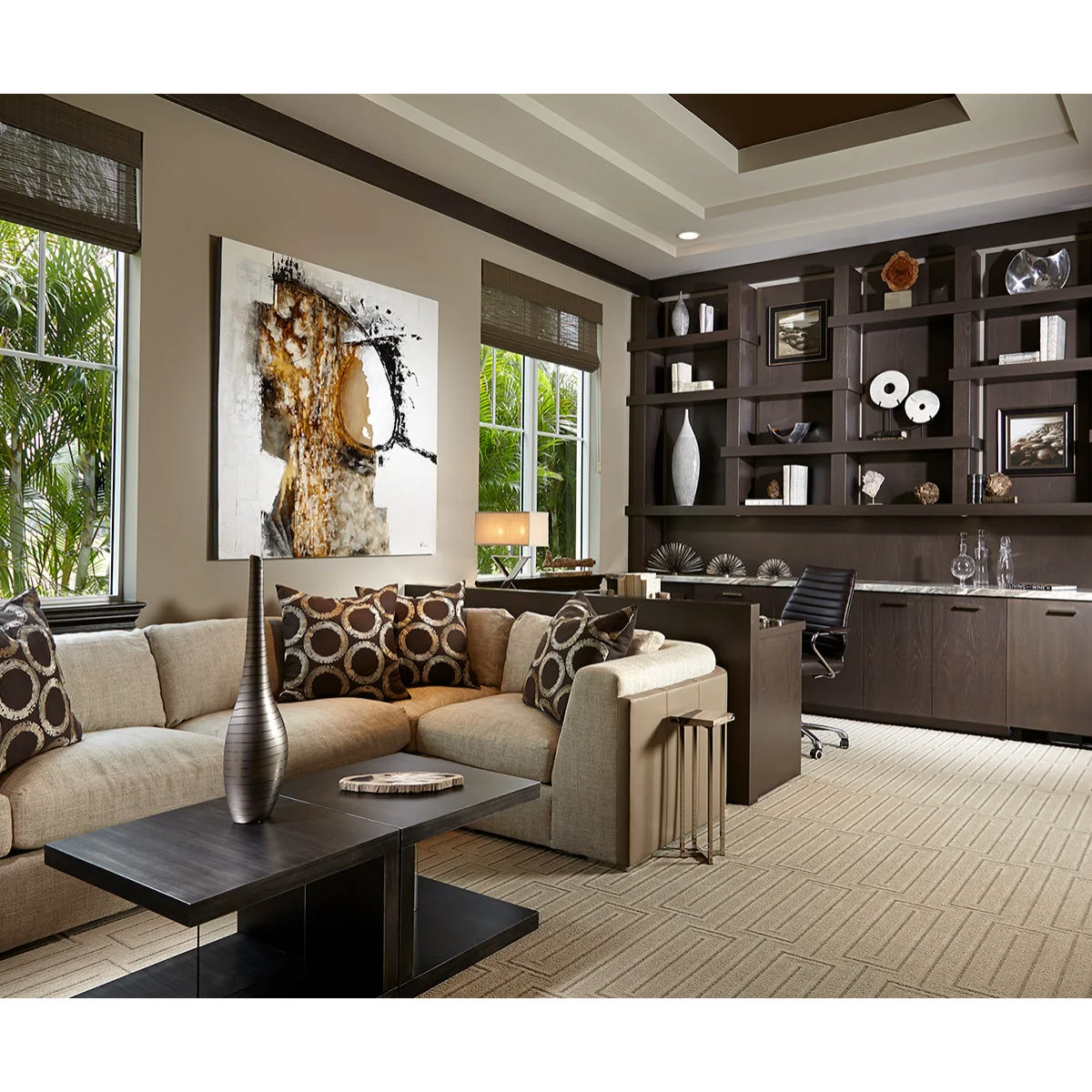 A dark desk and shelving wall behind a cream sofa and low coffee table in a pale-and-brown room.