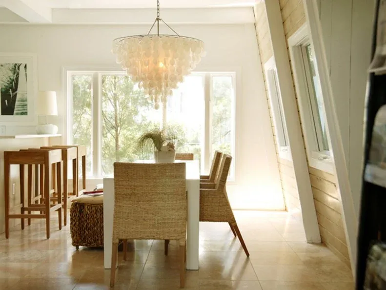 Pale dining room with woven chairs, light rectangular table, layered translucent chandelier and glazed doors behind.