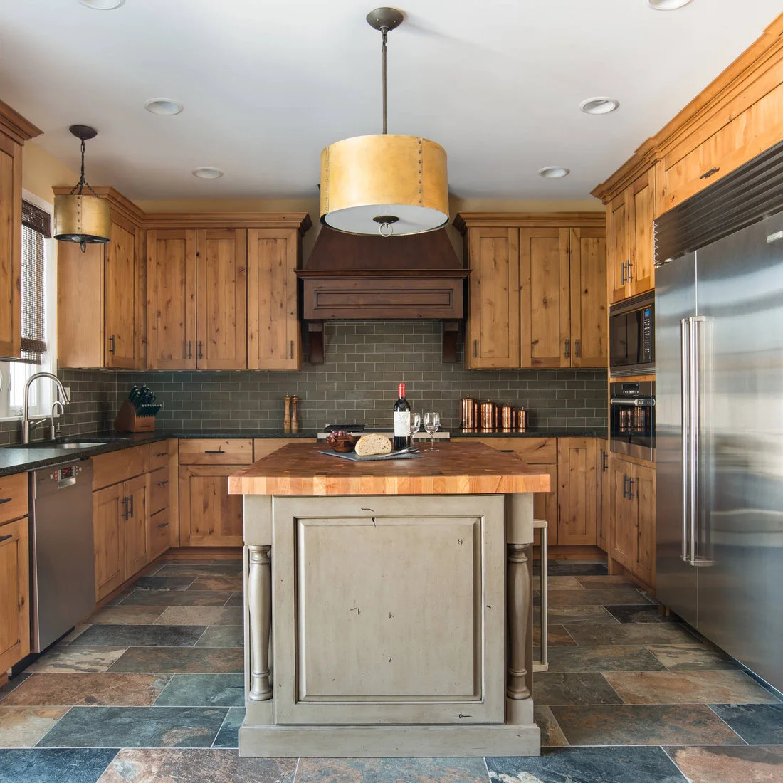 A small painted island with wood top surrounded by timber cabinets and a multicolored tile floor