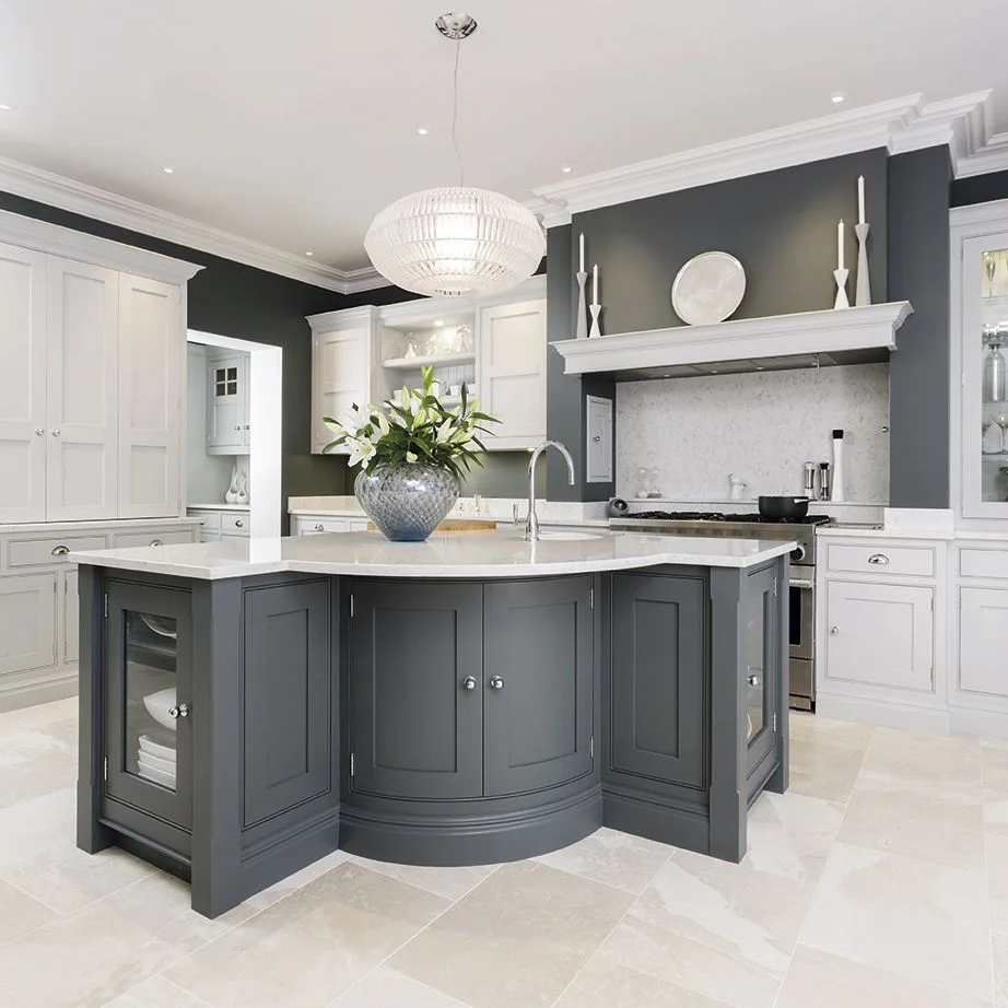 A dark gray paneled island with a curved end and open plate storage stands among white cabinets and a pale countertop