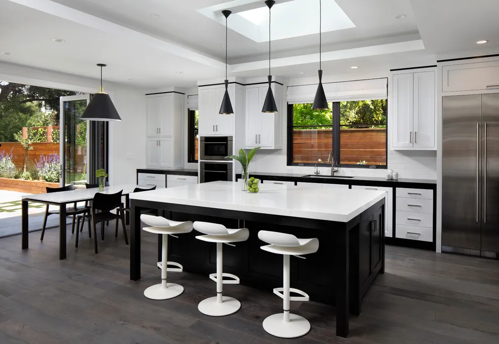A black island with a pale top sits in front of white cabinets and slim dark pendants