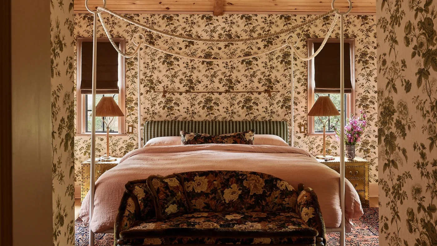 Brown flowering wallpaper around a canopy bed with pink bedding, a striped headboard and a wood ceiling.
