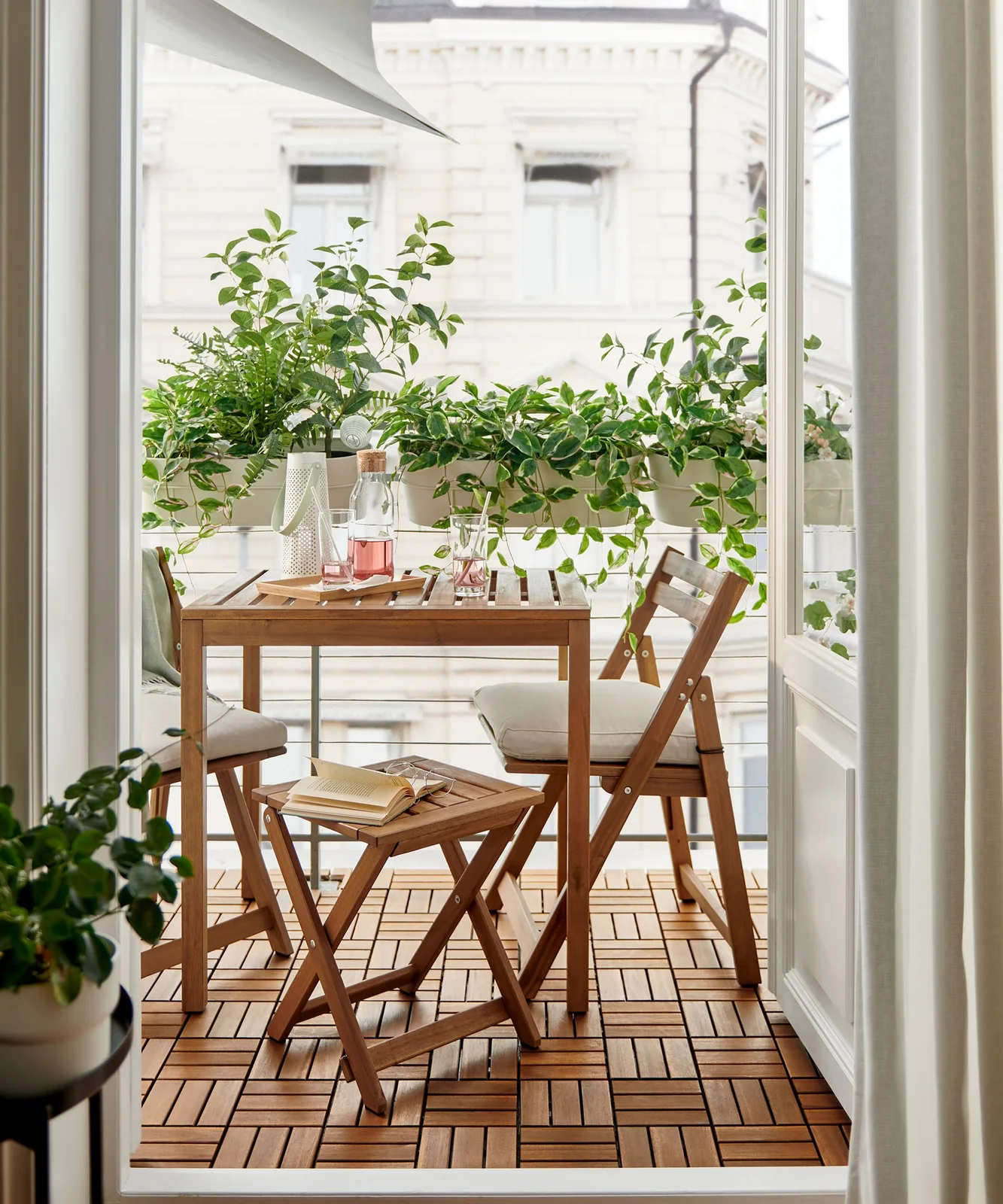 White railing planters with trailing greenery sit behind a small wooden balcony dining table