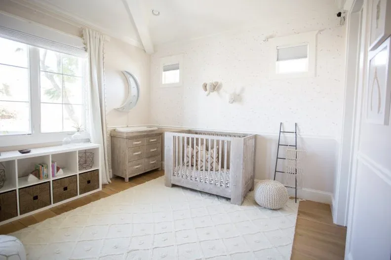 Light nursery with pale wood crib and dresser, white walls, window storage, baskets and subtle patterned rug
