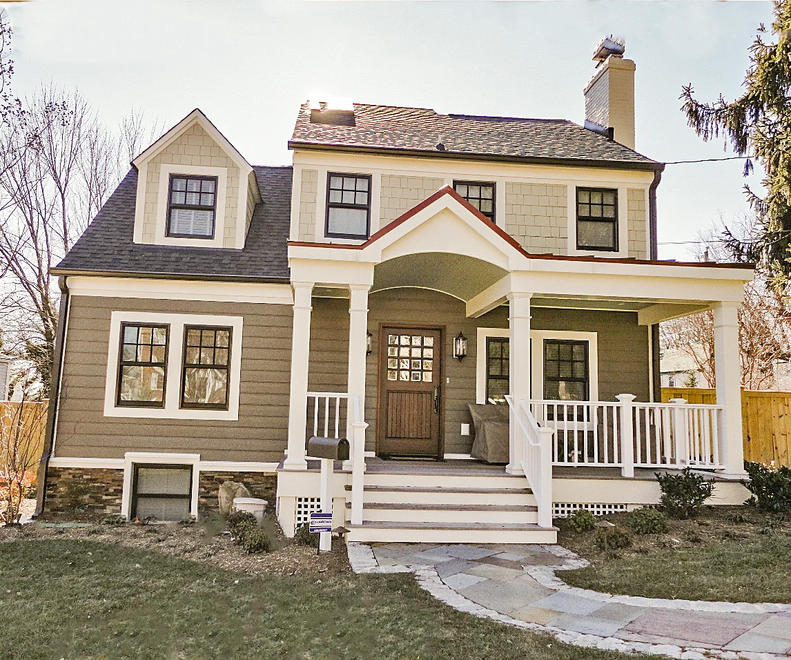 An expanded gray Cape has a white-railed porch, an arched central roof detail and a wood door above broad front steps.