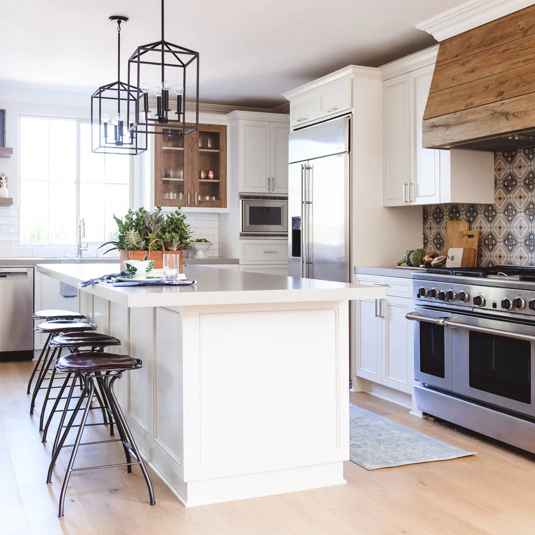 A patterned range backsplash and timber hood contrast with white cabinetry, black lantern pendants and a pale island.