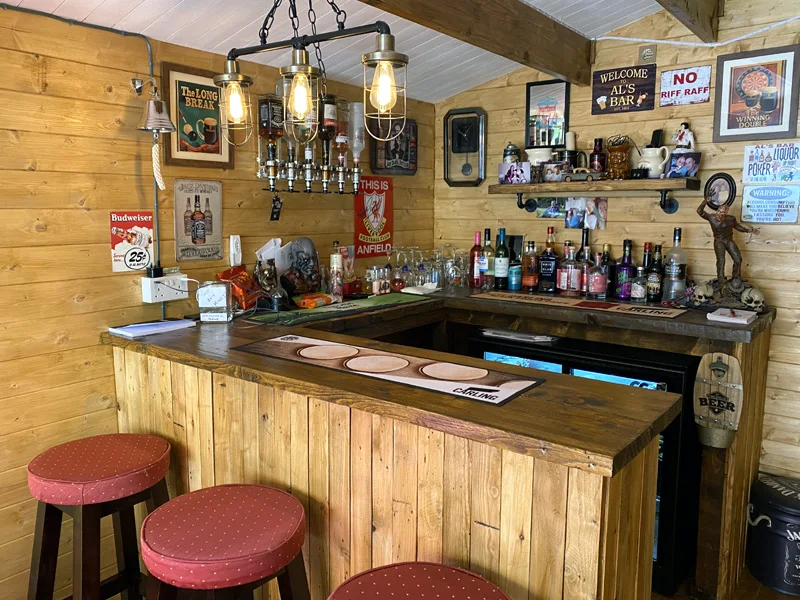 Wood shed pub with a U-shaped bar, red stools, bottle shelves and hanging caged lights