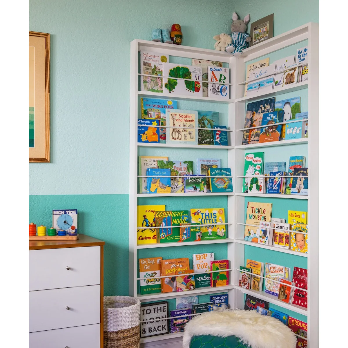 White corner book shelves displaying colorful covers against a turquoise nursery wall