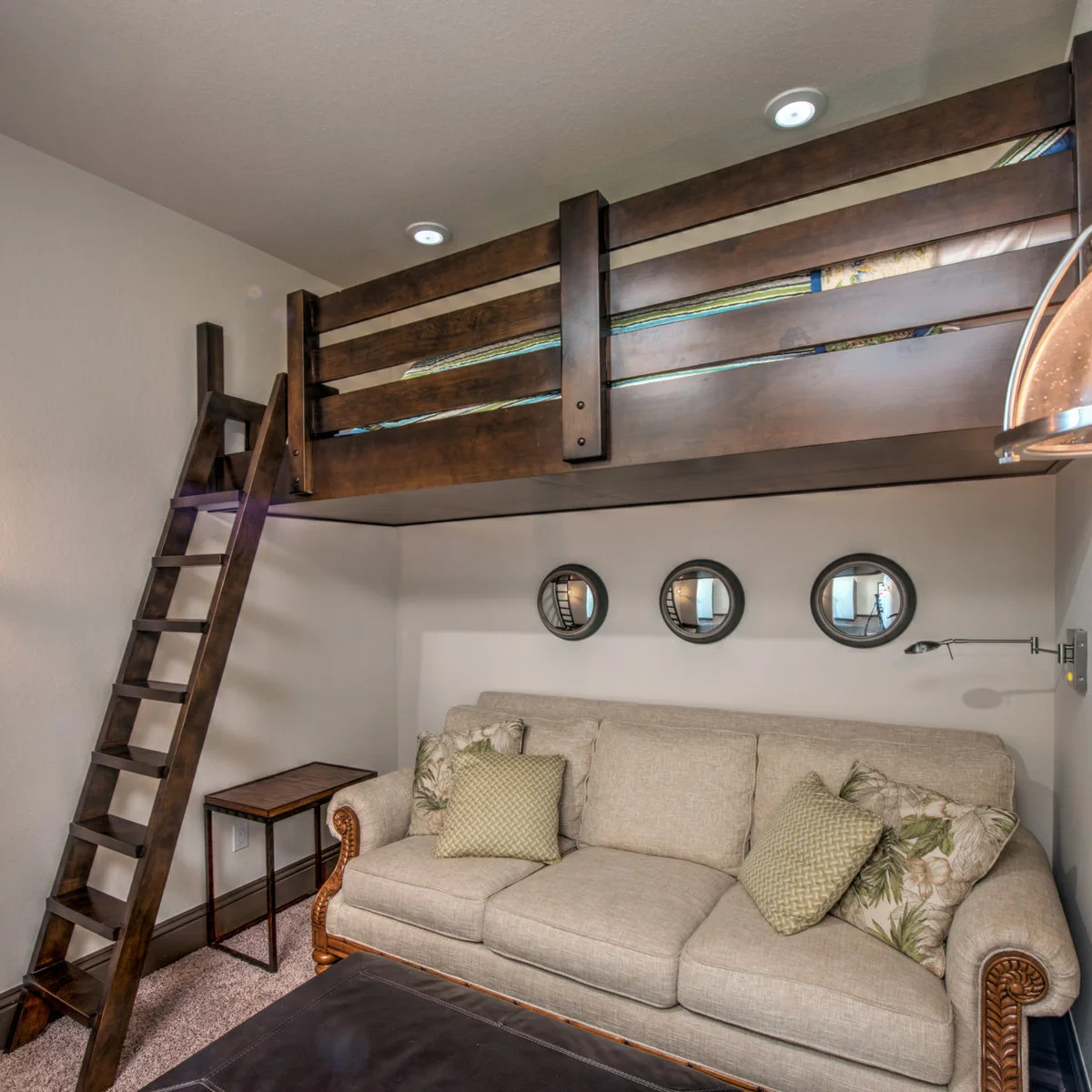 Dark wood loft bed above a cream sofa with three round mirrors on the wall and a ladder at the left.