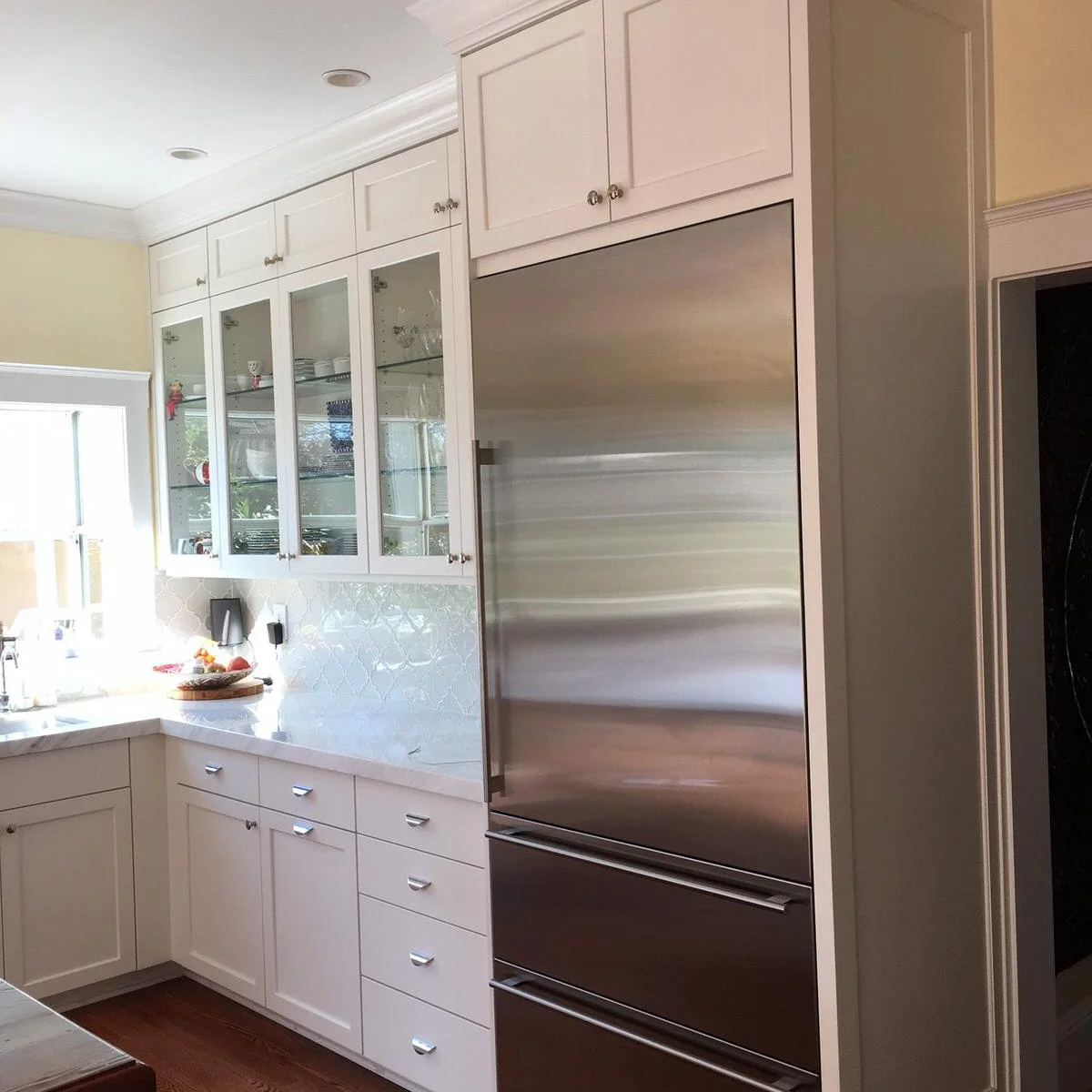 A white cabinet above a stainless refrigerator aligns with the small upper doors over neighboring glass-front cupboards.