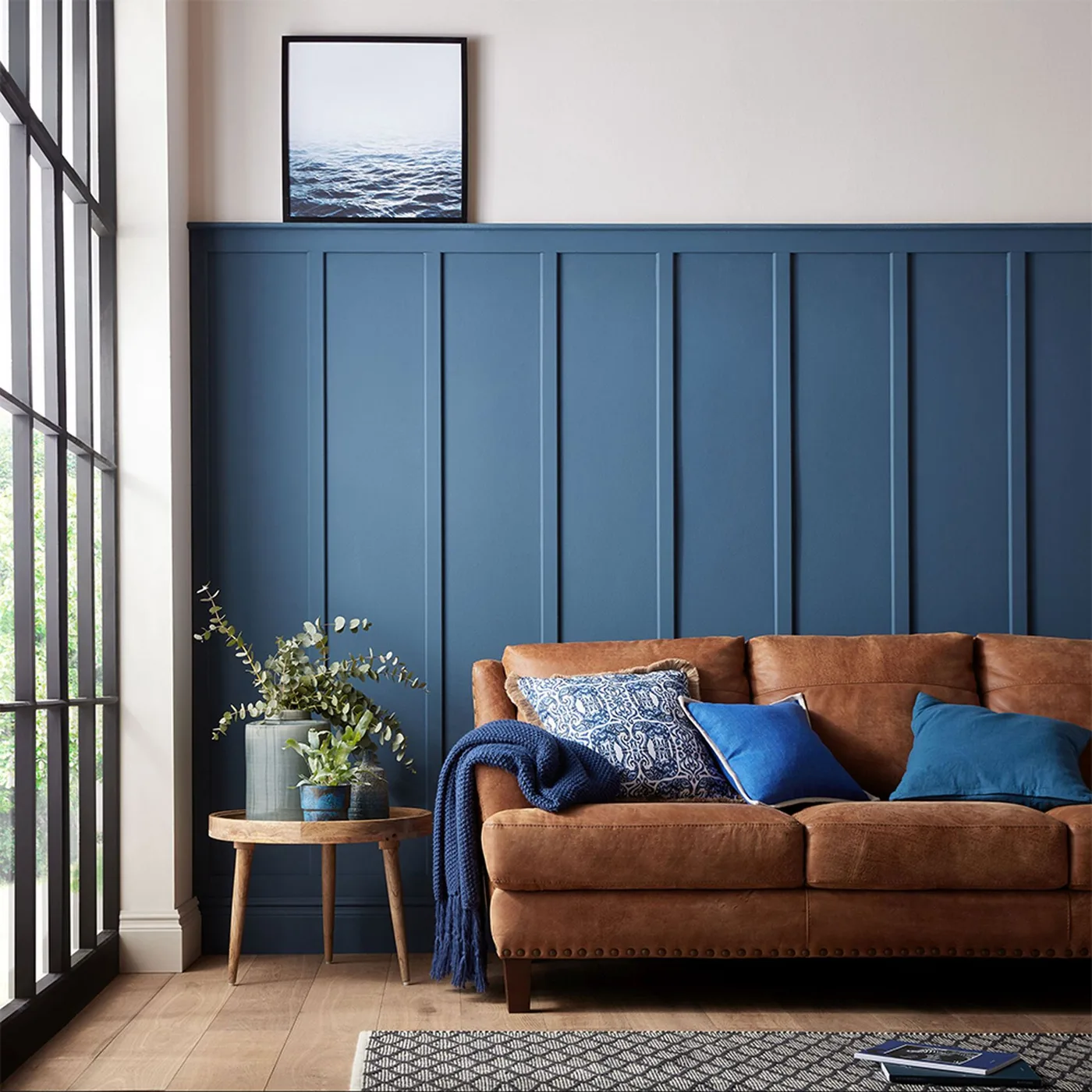 Brown couch with patterned blue-and-white pillow, bright blue square and darker blue pillow beneath blue paneling.