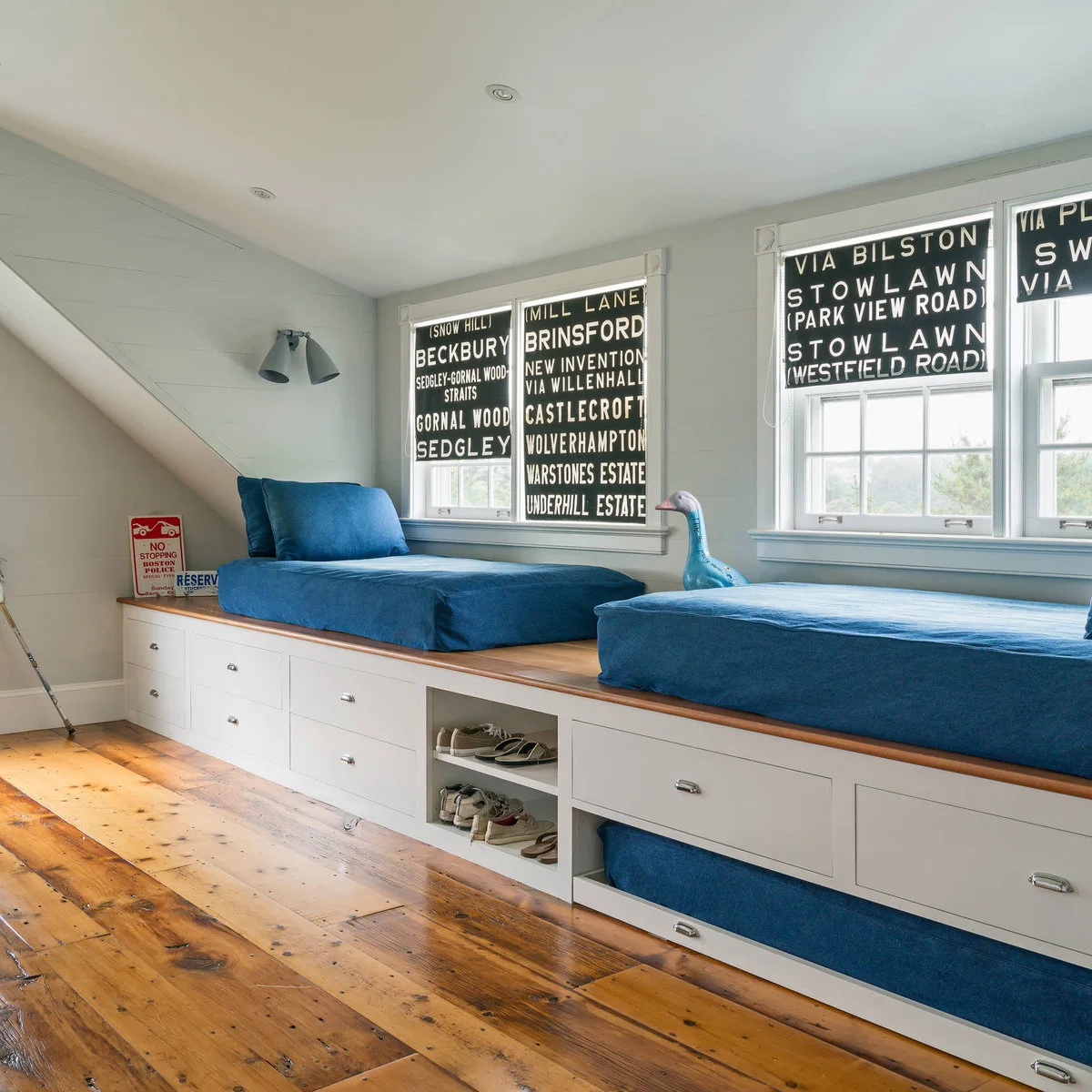 Two blue cushioned beds on a continuous white drawer platform with shoe cubbies between them