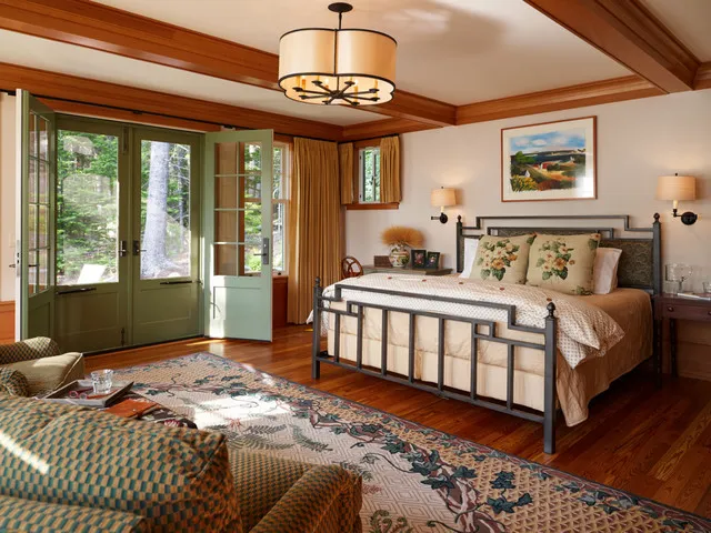 A dark metal bed stands in a timber-trimmed room with patterned pillows and a substantial rug.