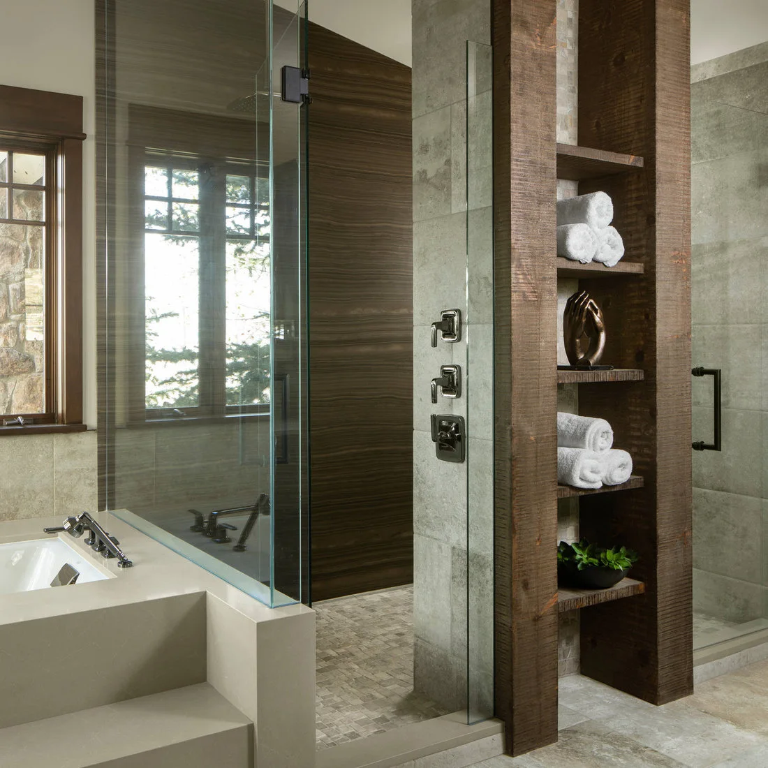 A tall timber towel shelf between glass shower enclosures beside pale tiled surfaces