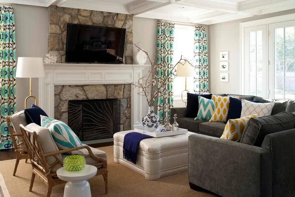 Dark gray seating is surrounded by light upholstery and patterned curtains near a stone fireplace