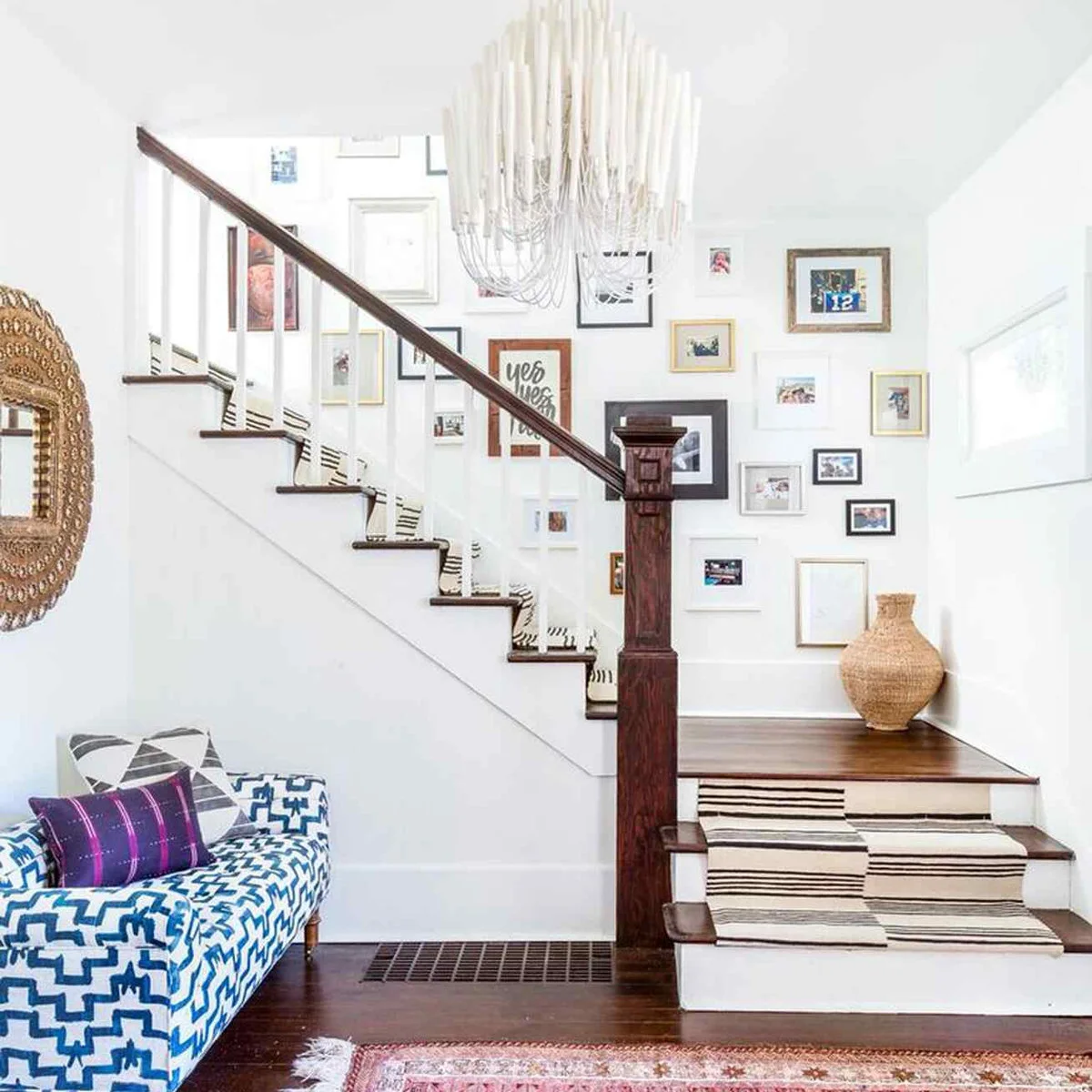 Mixed black, white and gold frames climb a white stair wall above a striped runner.