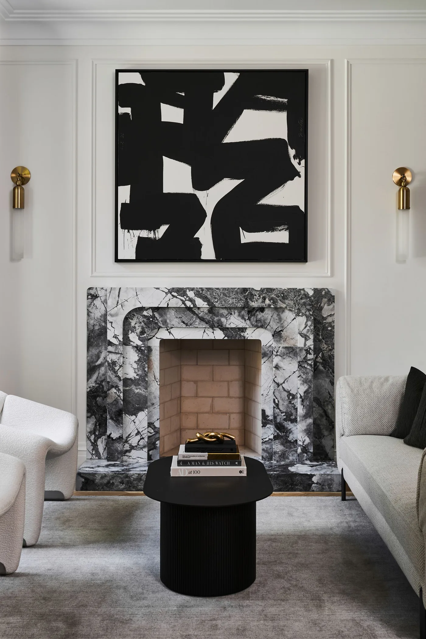 A black-and-white veined fireplace surround sits beneath abstract artwork between gold-toned wall lights and pale seating