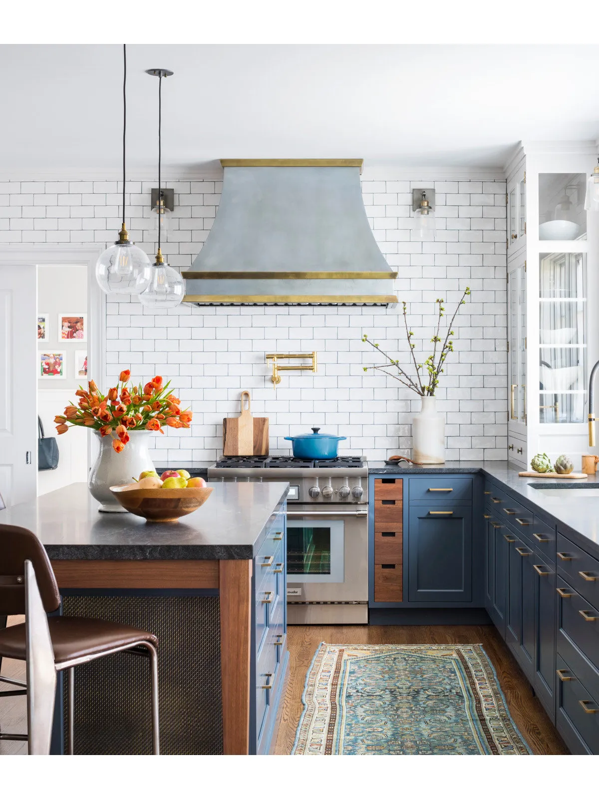 Blue cabinetry sits beneath a pale hood and tile wall beside a narrow patterned runner.
