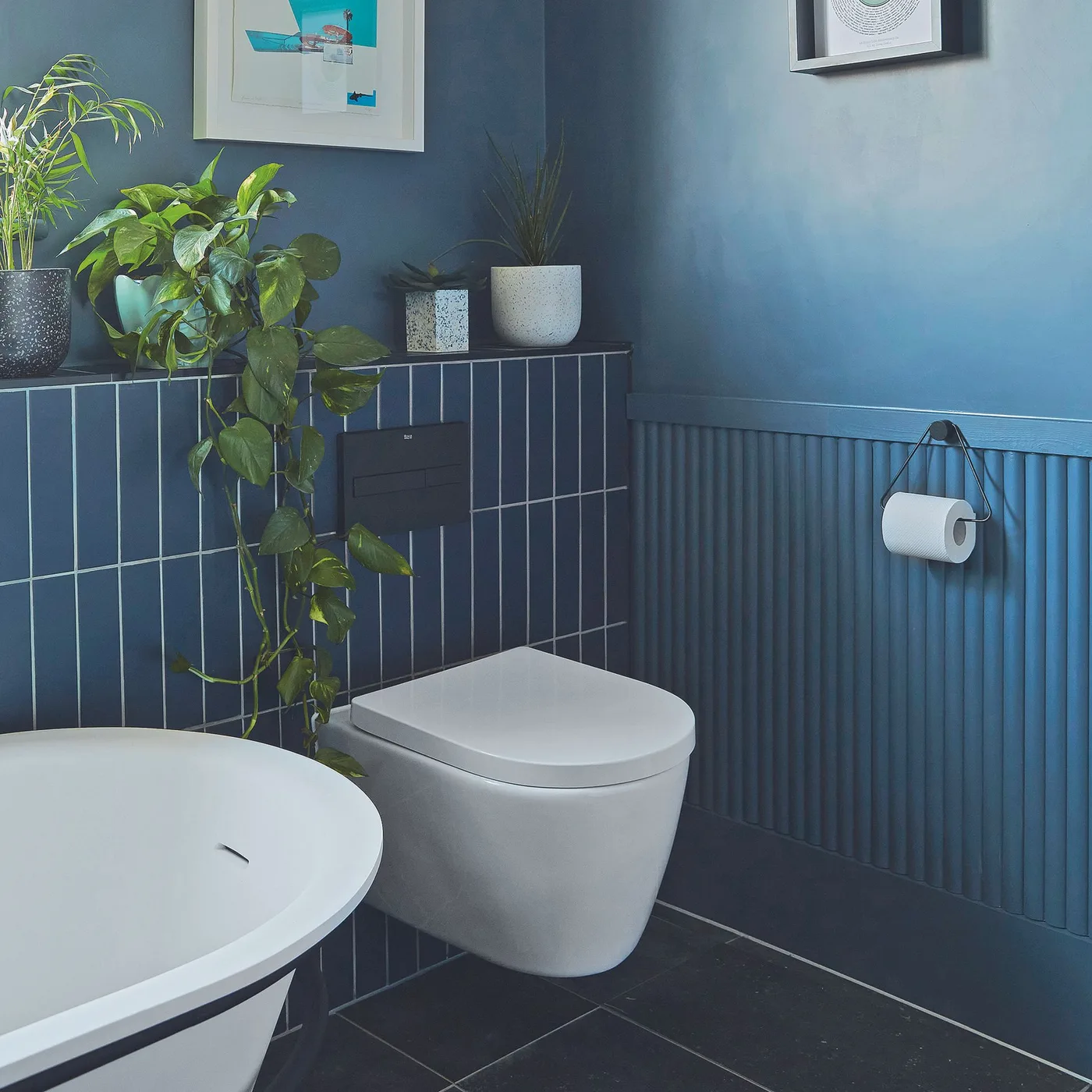 Deep blue tiles and ribbed paneling meet beside a white wall-hung toilet and a curved bath edge