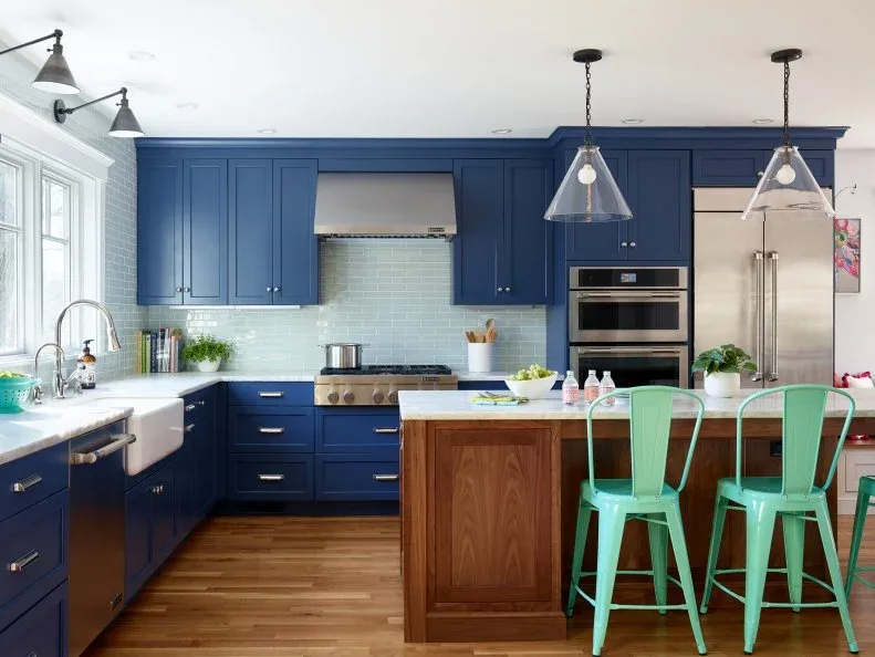 Pale blue-green rectangular backsplash tiles sit between blue cupboards and light counters beside a wooden island and mint dining chairs