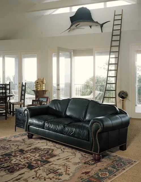 A black rolled-arm leather sofa with nailhead trim sits on a patterned rug beneath a high pale ceiling