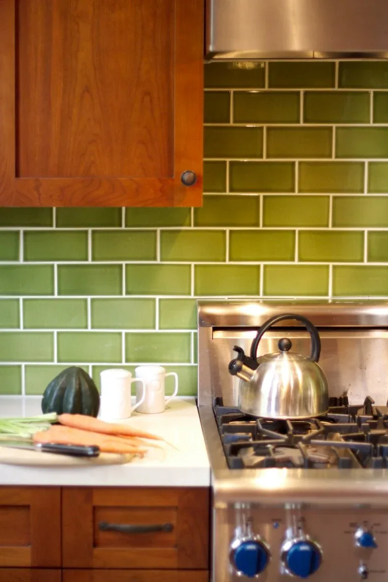 Glossy green rectangular backsplash tiles with light grout sit beside wooden cupboards and a metal cooker