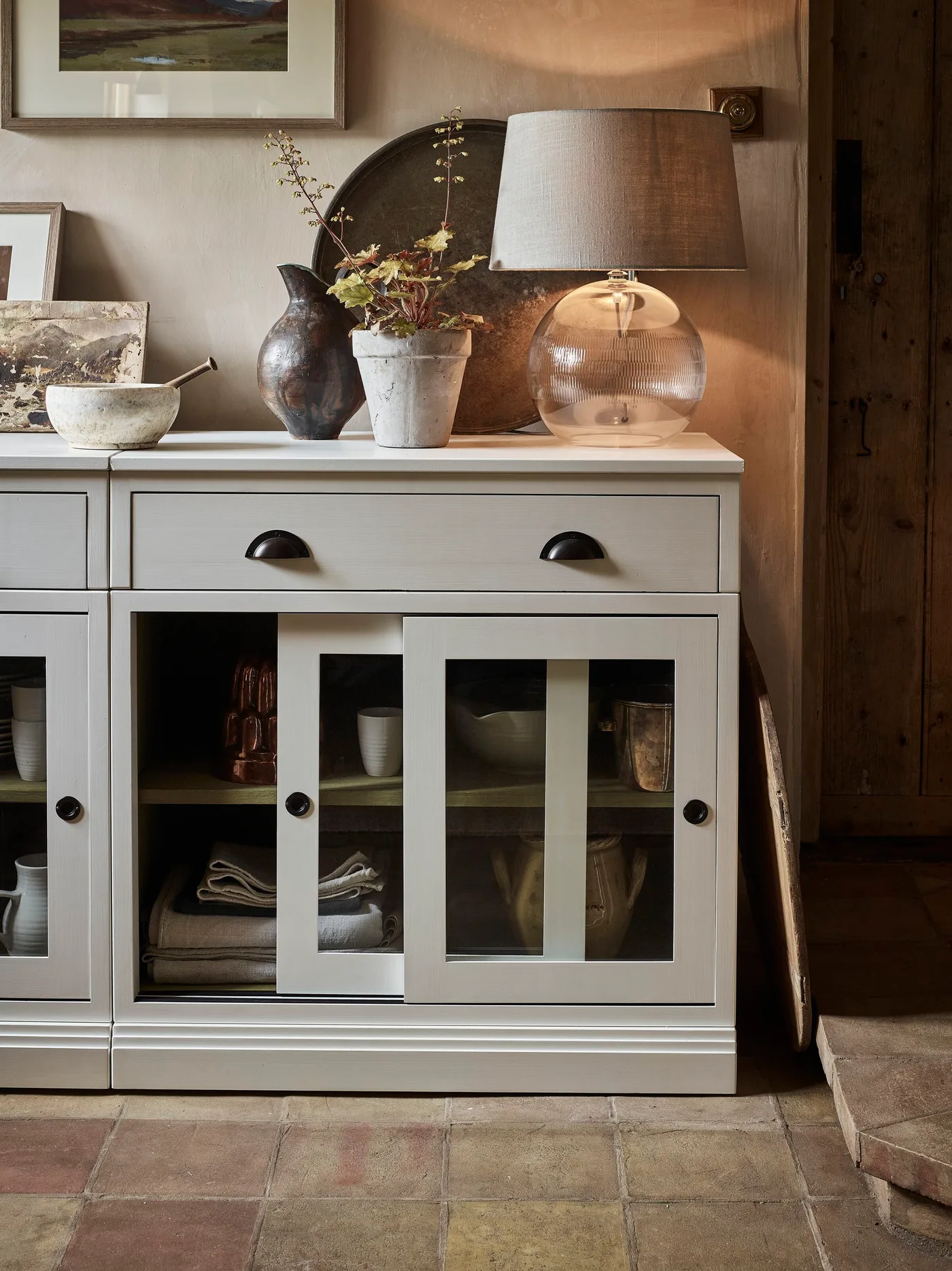 Gray glazed sideboard with a dark round backdrop, lamp, bowls and vases on a tiled floor