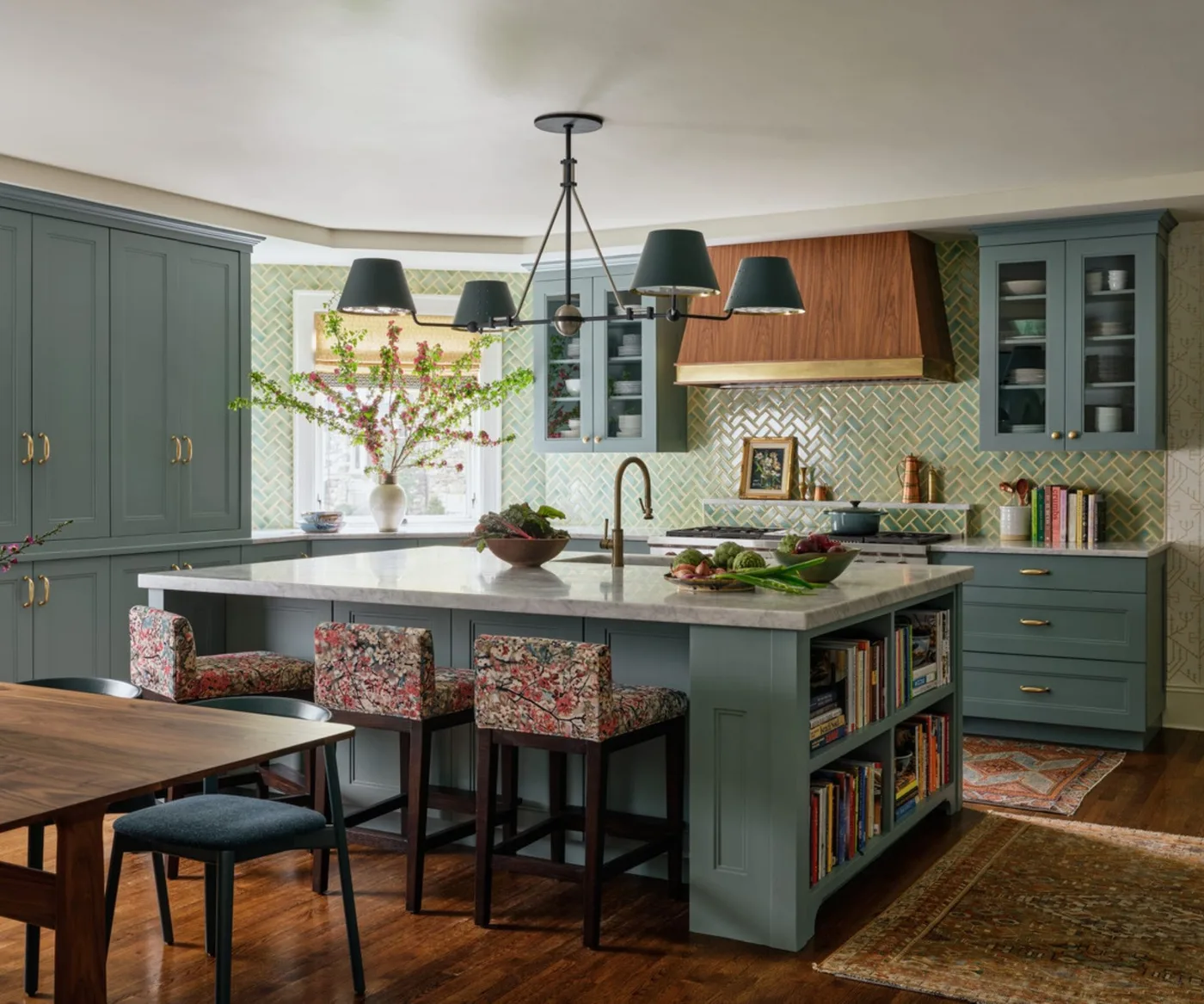 Pale green herringbone tiles surround a wood-clad hood behind blue-green cupboards and a large island with patterned stools