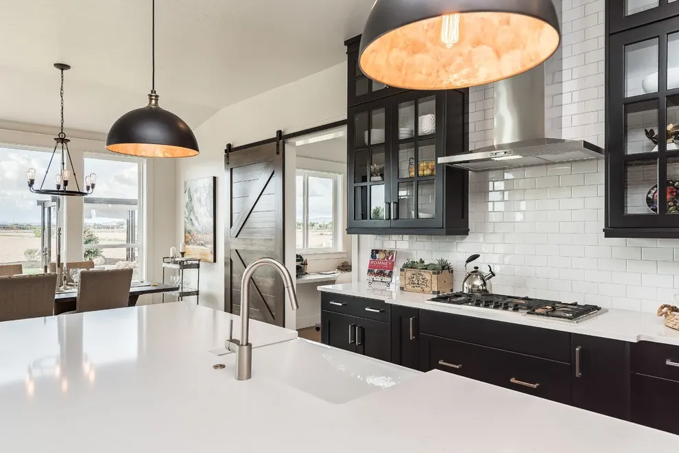 Dark lower cabinets sit beneath pale counters beside black pendants with warm-toned interiors