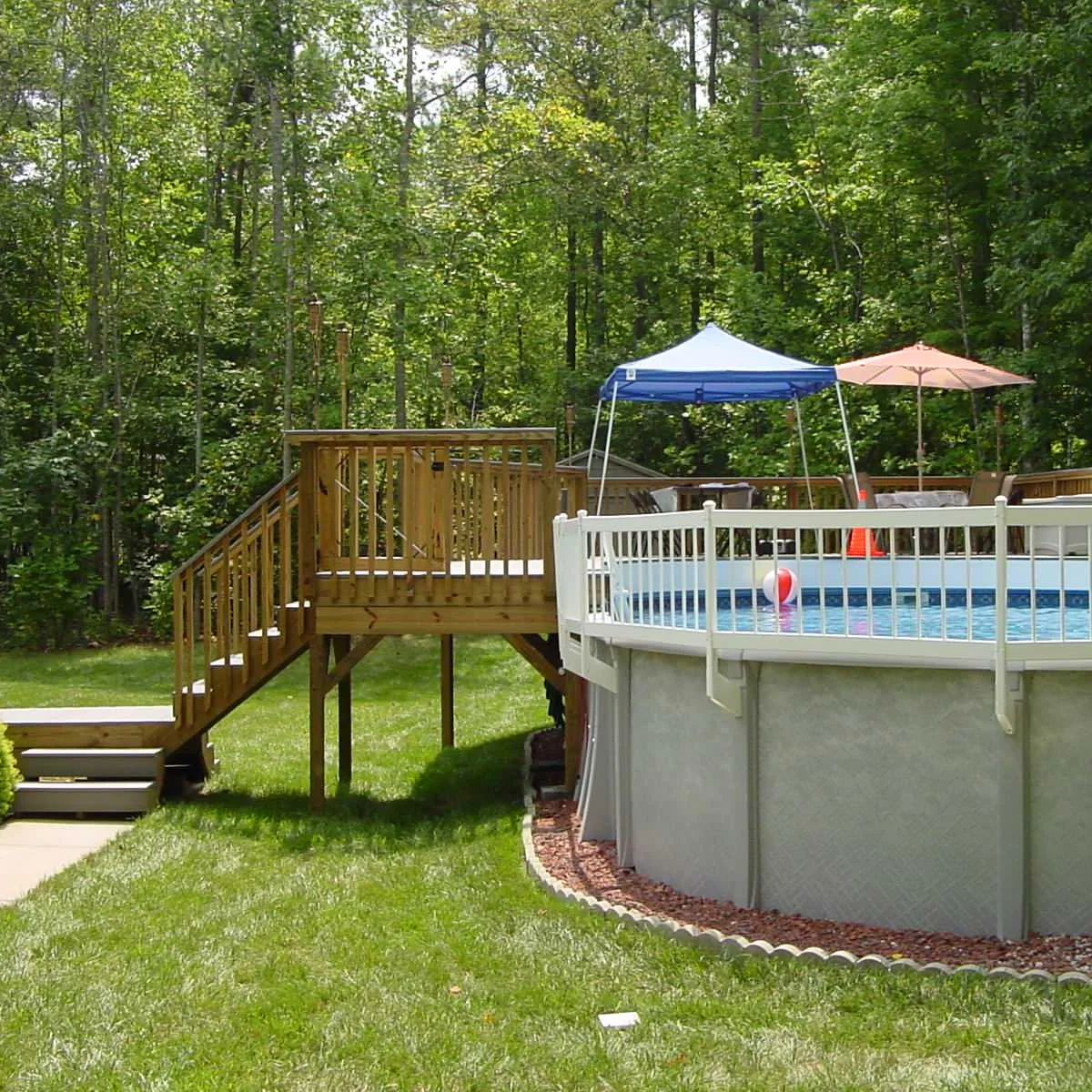 Round above-ground pool with white railings along the exposed edge and a raised wood deck reached by stairs.