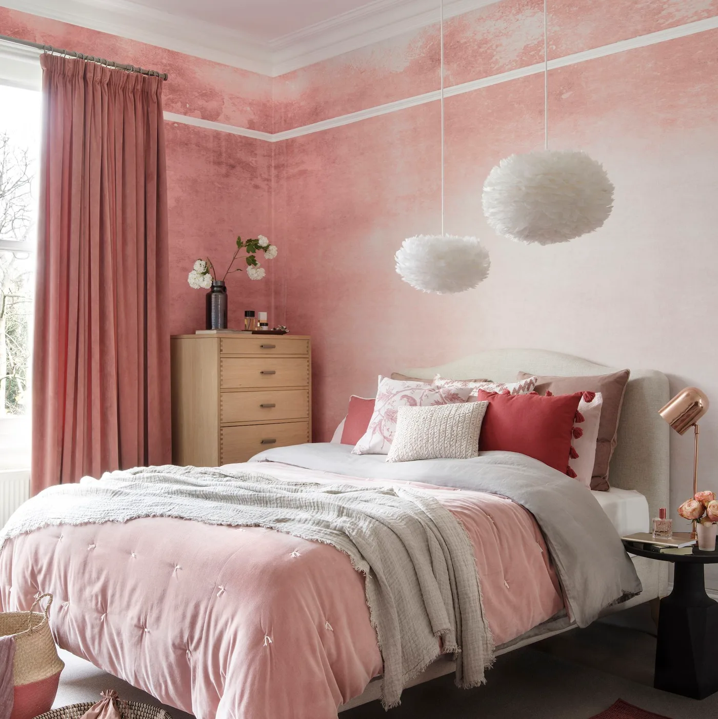 Dusty pink bedroom with mottled walls, long pink curtains, a rose bedcover and two fluffy white pendants