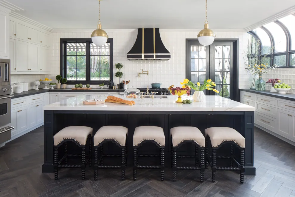 A dark island sits beneath a pale counter beside white cabinets and black-framed windows
