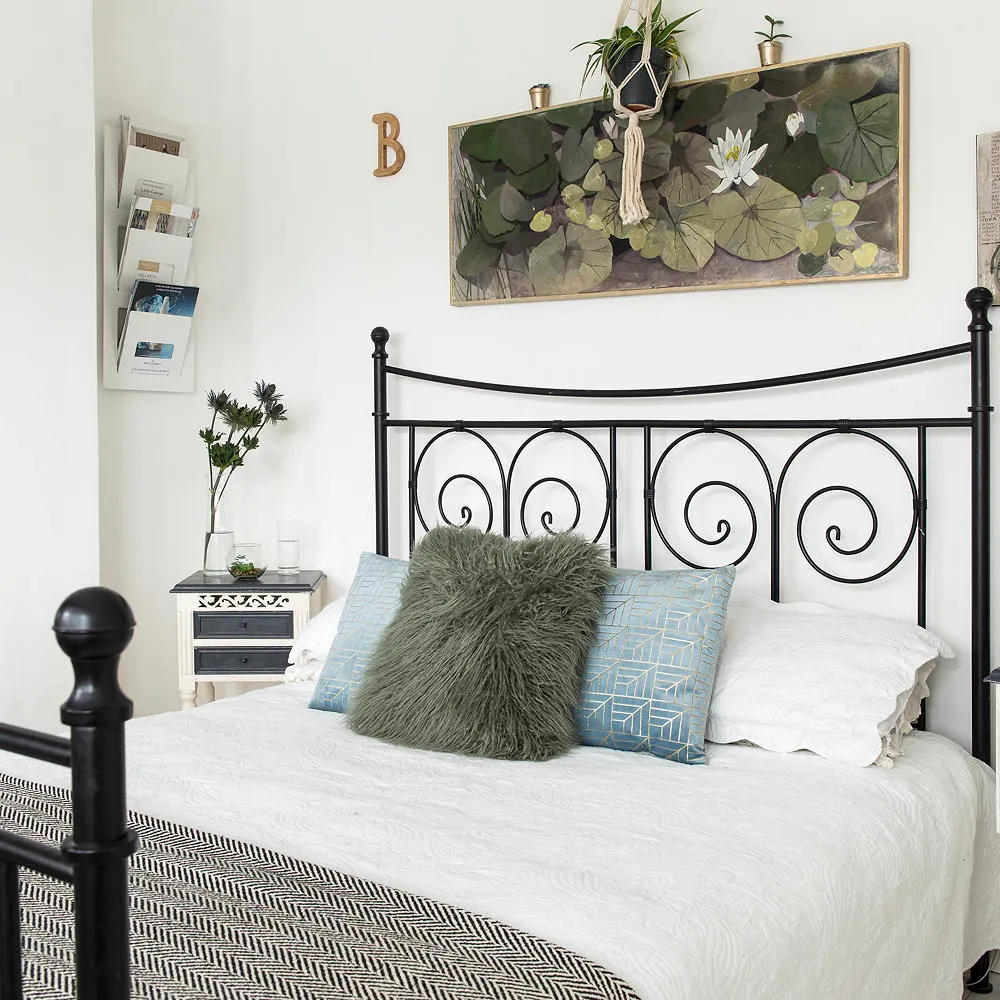 A black scrollwork bed stands against white walls with pale bedding and green cushions