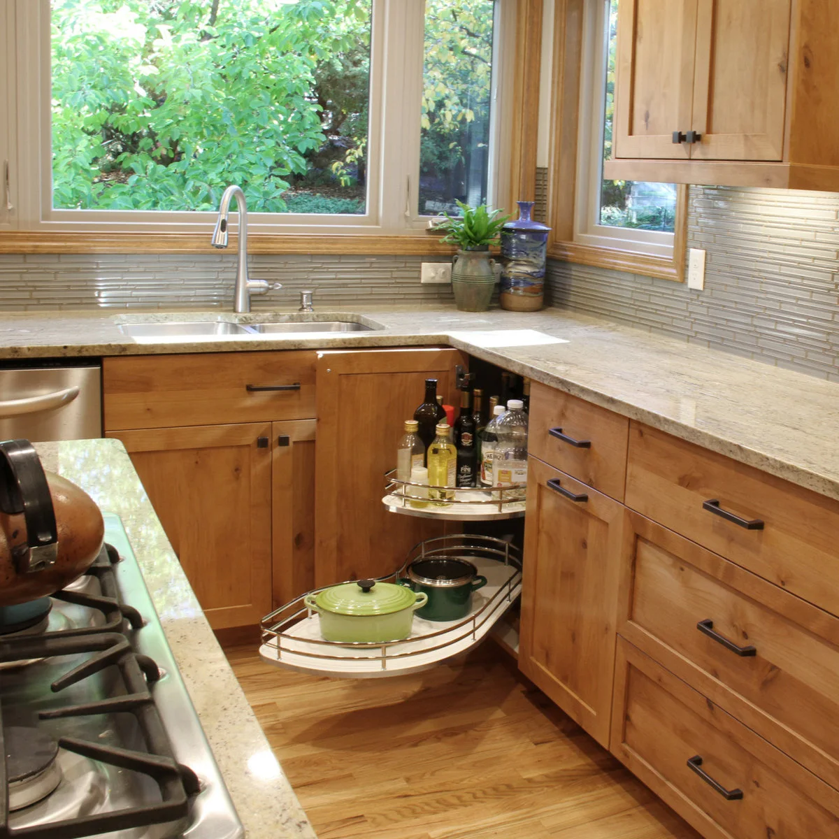 Wooden corner cabinet with curved swing-out shelves holding bottles above green cookware