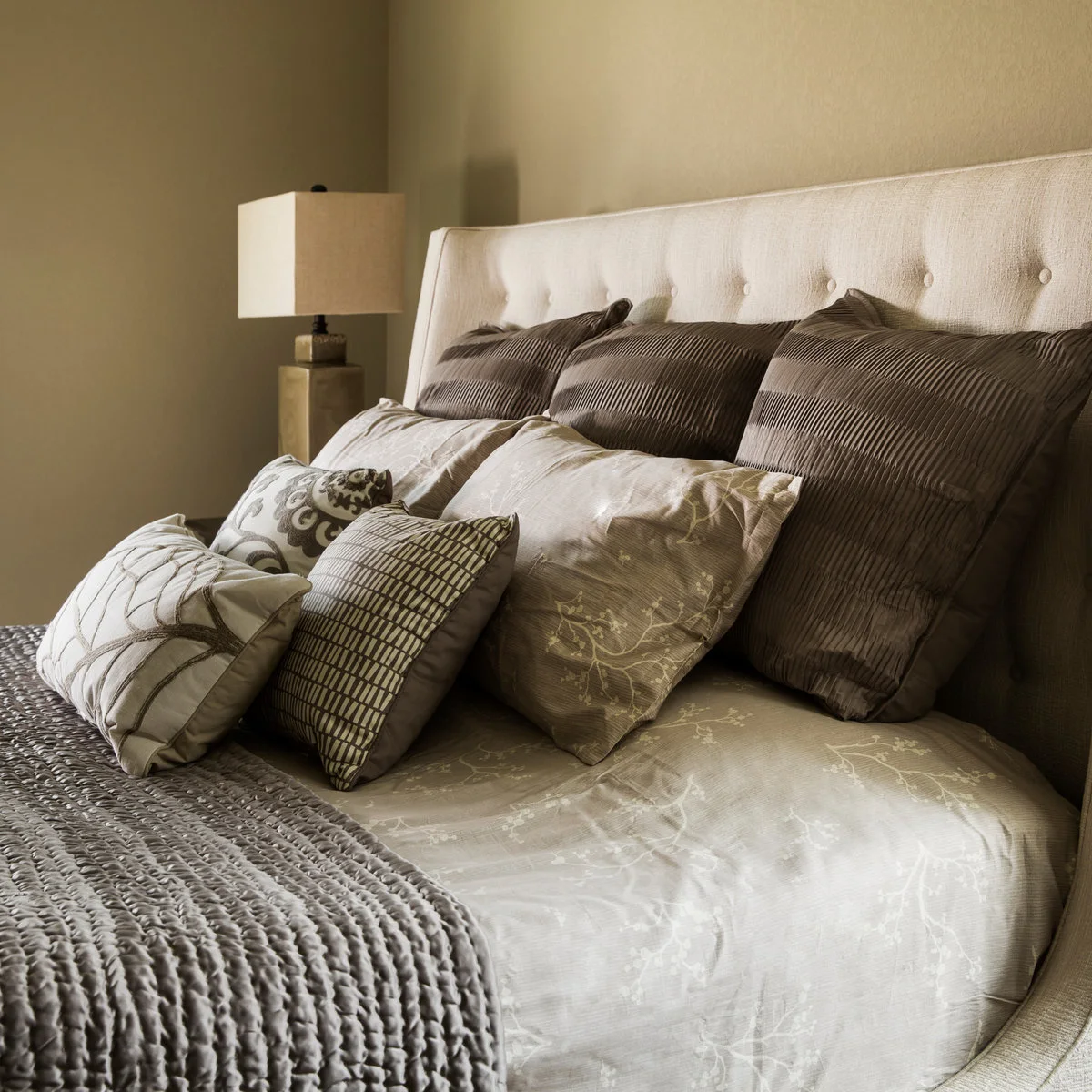 Close view of cream headboard with brown pillows, muted floral bedding and a textured throw