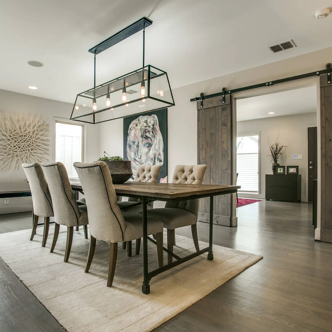 Pale rectangular rug beneath a wood dining table and tufted chairs beside a sliding wood door
