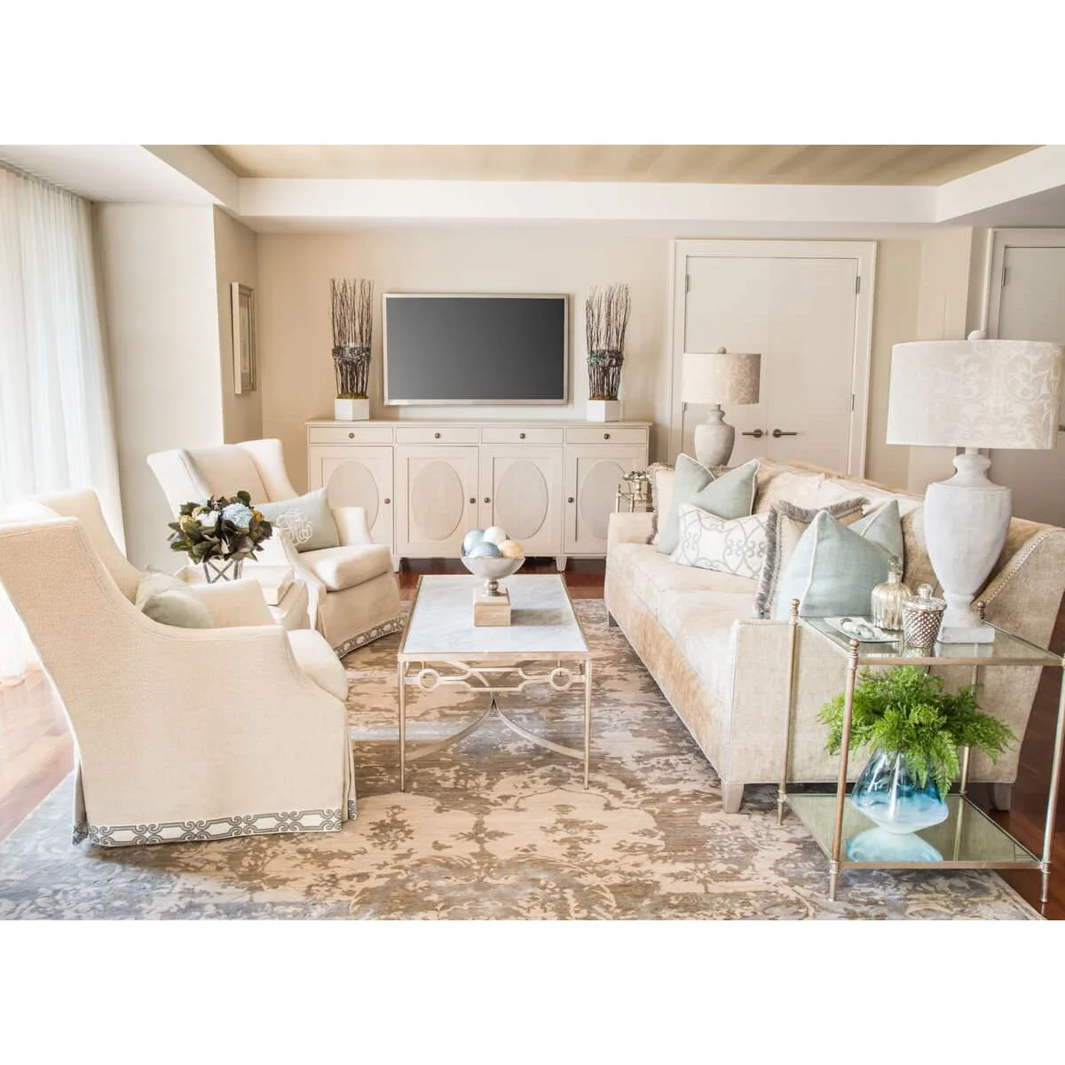 Matching twig arrangements in pale square containers flank a television above a cream cabinet with oval door details.