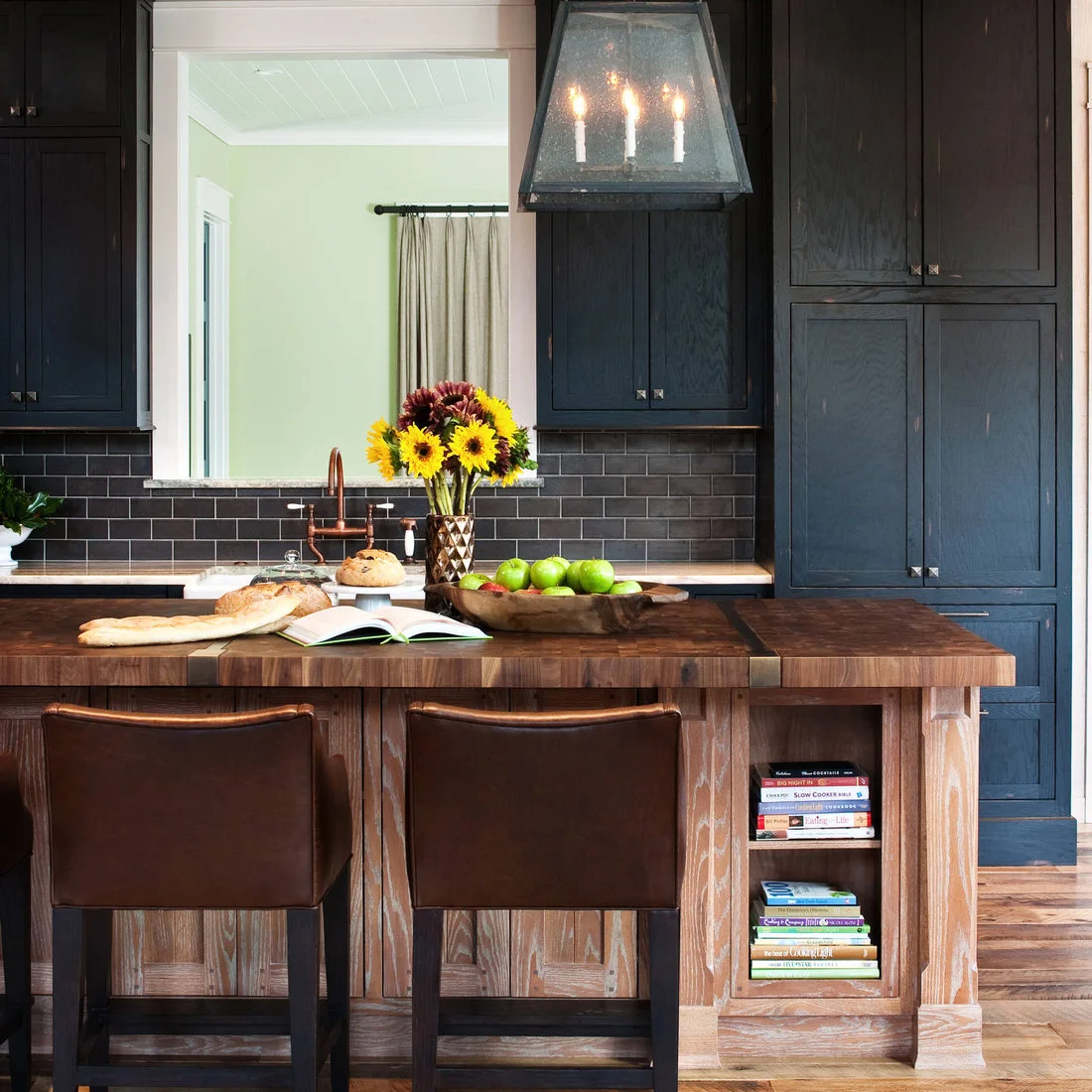 A wood topped island with an open cookbook shelf in front of dark blue cabinets
