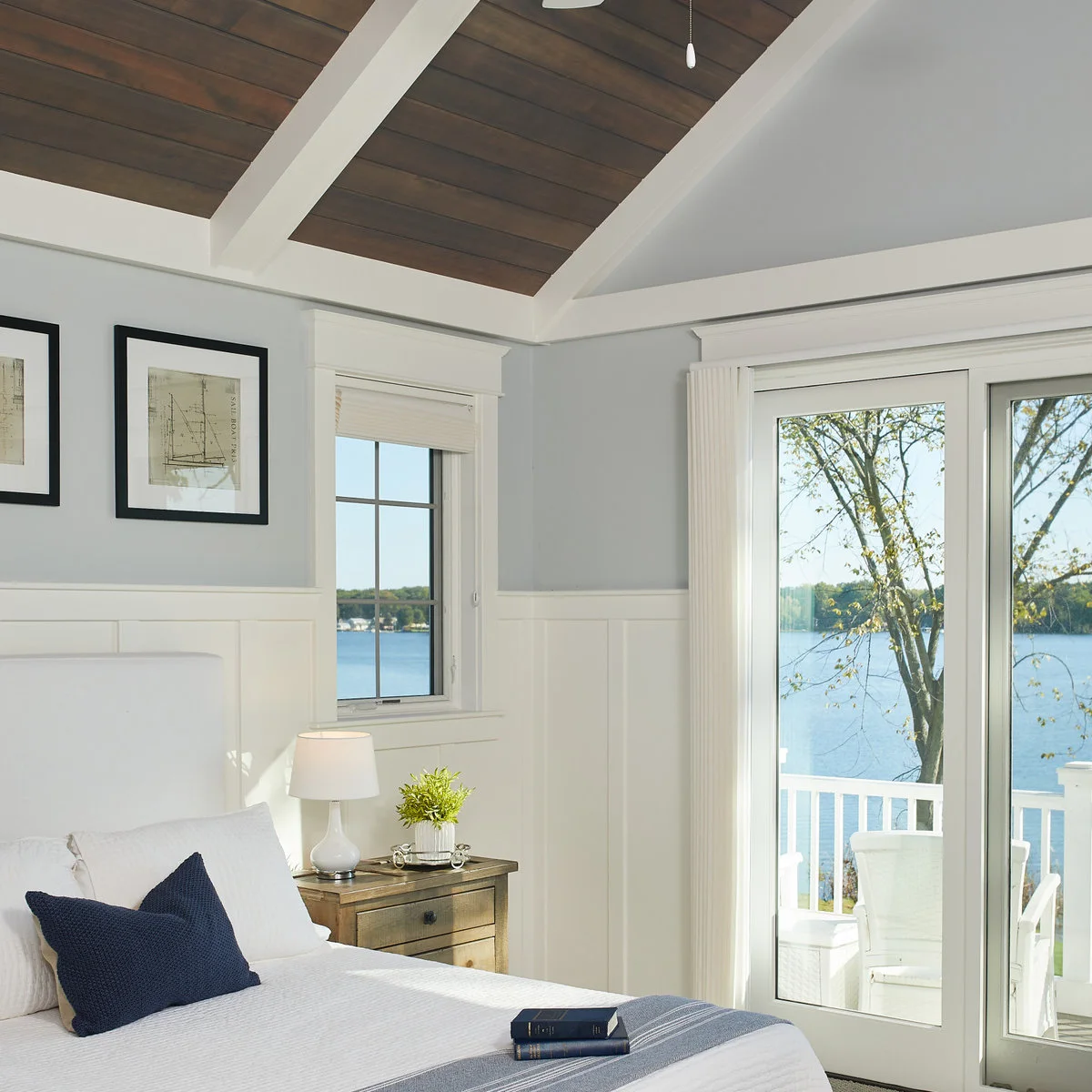 Pale grey upper bedroom walls above white lower paneling beside a wood nightstand