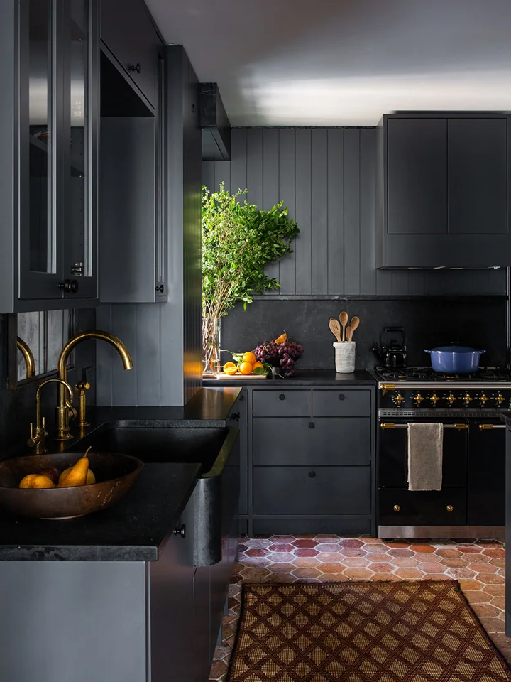 Rust-colored hexagonal floor tiles brighten the base of a charcoal kitchen with a patterned mat.