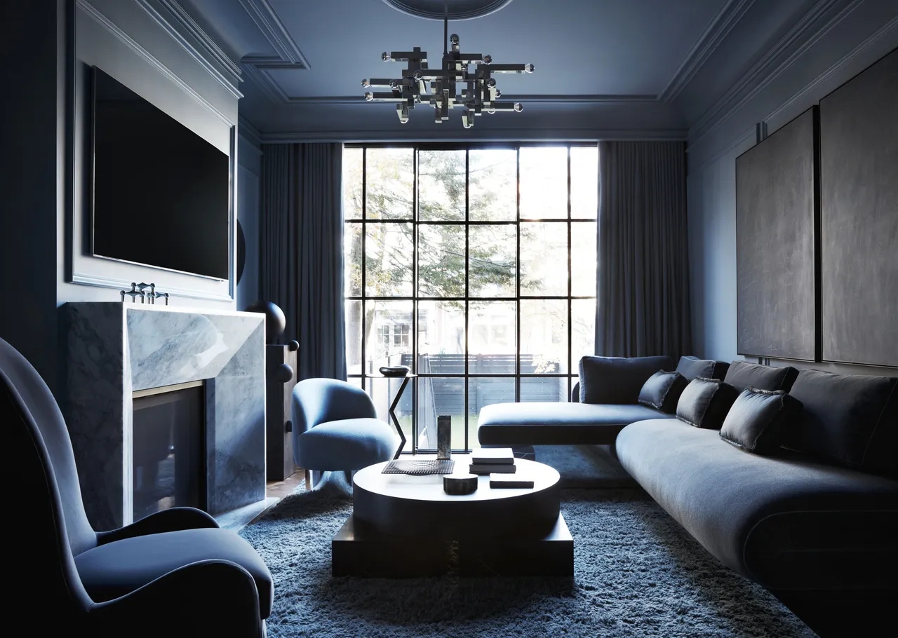 A dark gray sofa sits against charcoal paneled walls beside a bright window