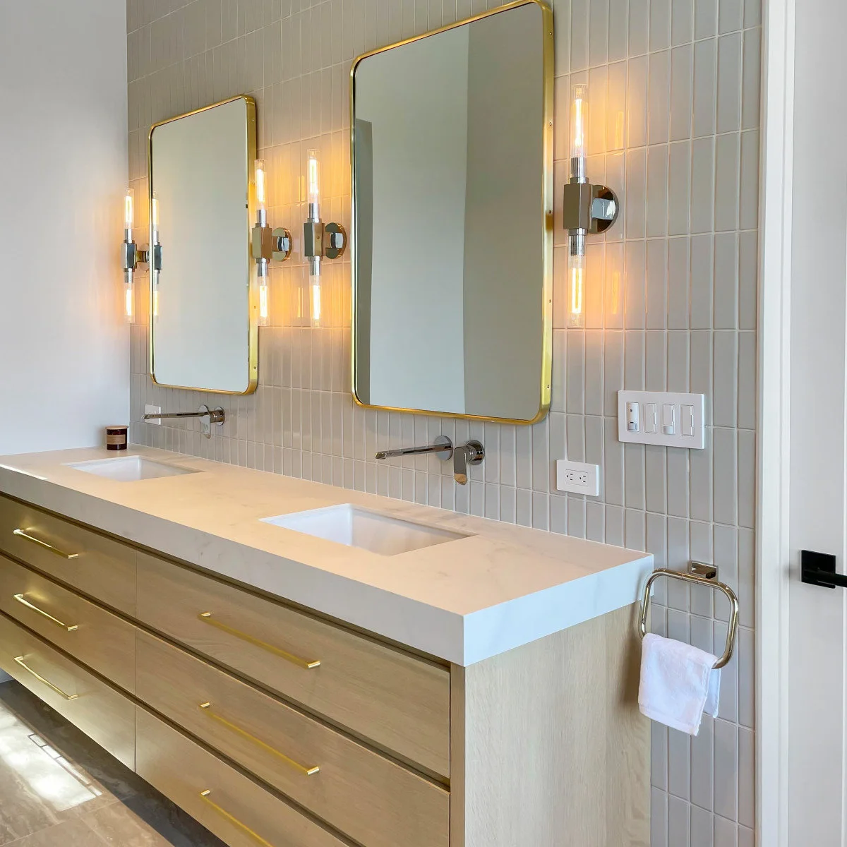 Gold-colored rounded rectangular mirrors with vertical lights above a double vanity
